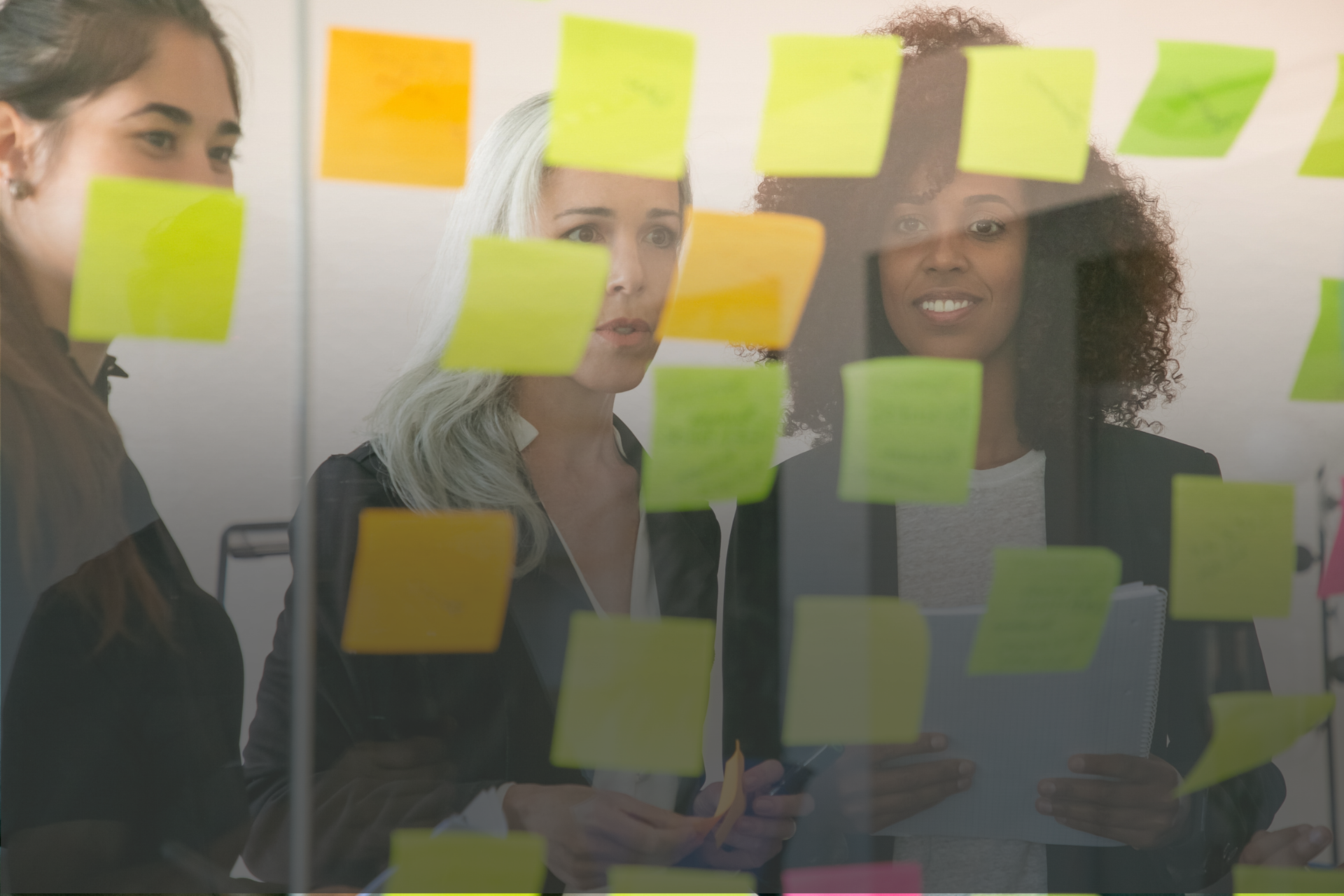 mulheres olhando para um quadro cheio de post its coloridos