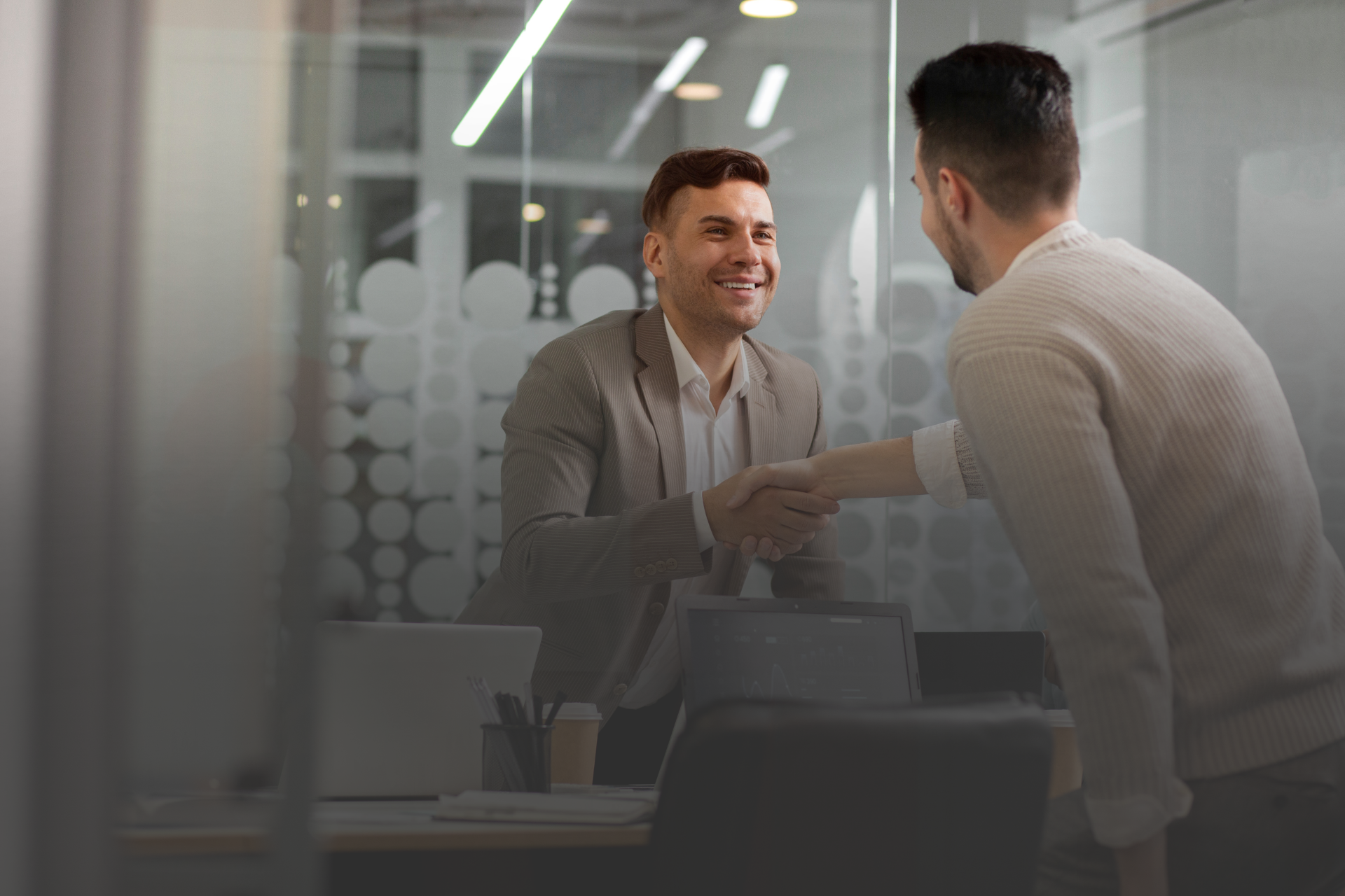 Dois homens em pé dando um aberto de mãos em uma ambiente corporativo